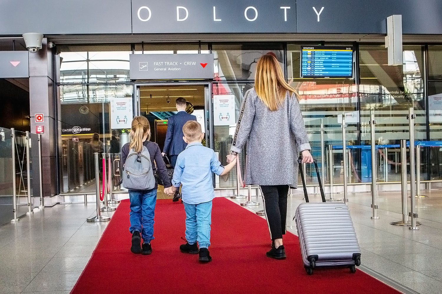 A woman with a suitcase and two children walks toward the fast-track security lane.