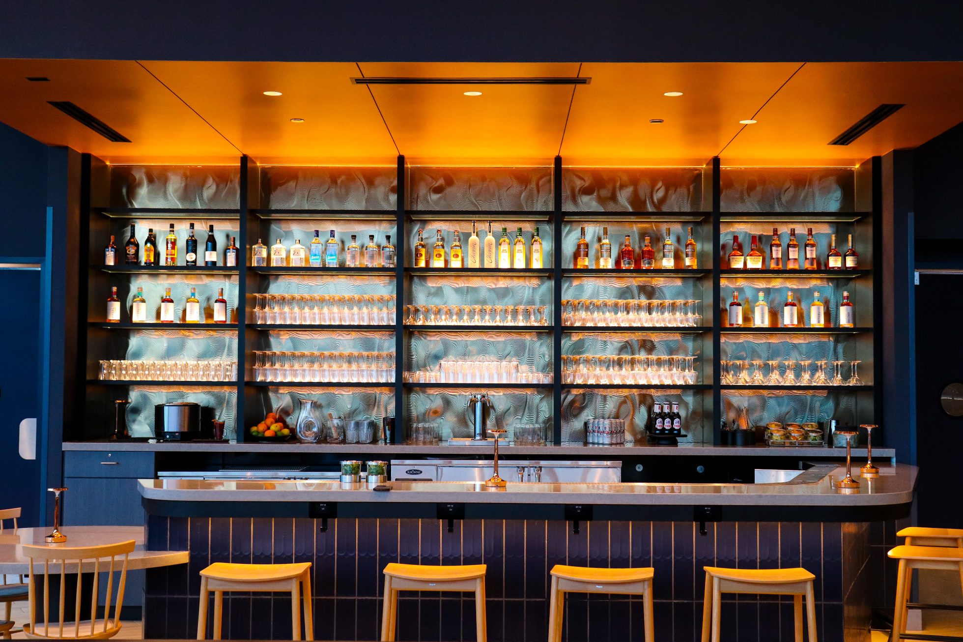 Front view of illuminated bar - bar stools in front, illuminated bottles on bar shelves in back