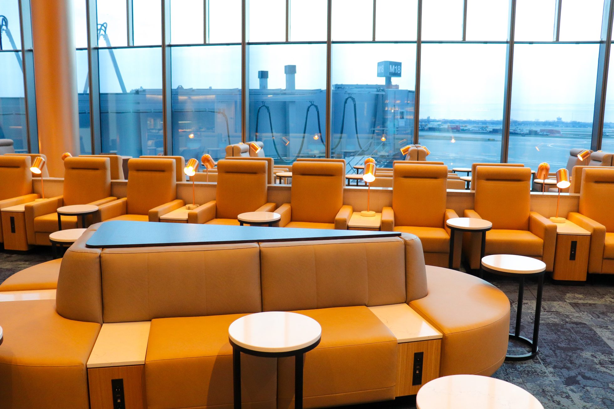Beige sofas, armchairs and coffee tables in the back, panoramic window with view of the airport tarmac in the Business Lounge in Chicago