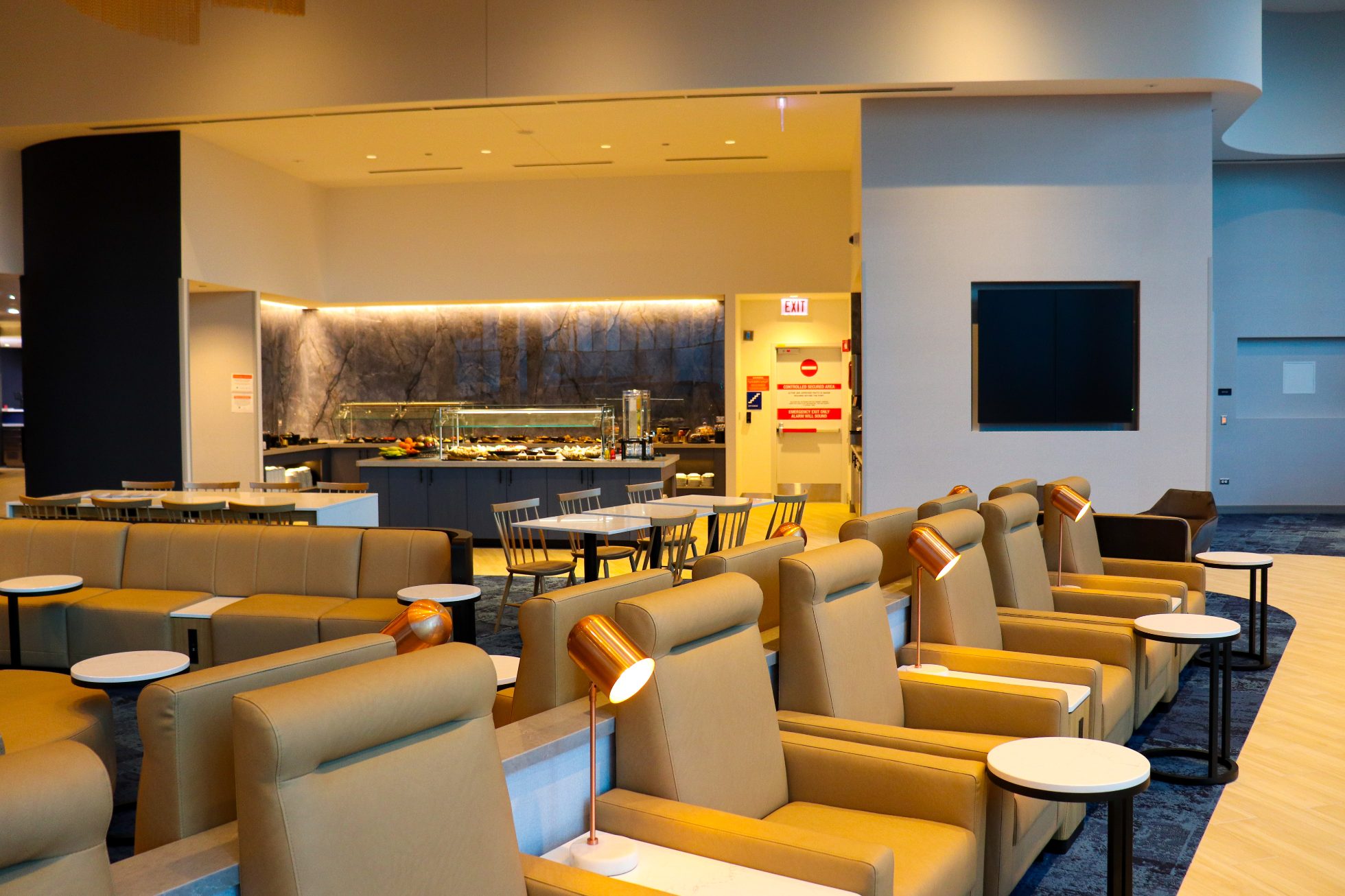 Row of beige armchairs with coffee tables, dining area visible in the background.