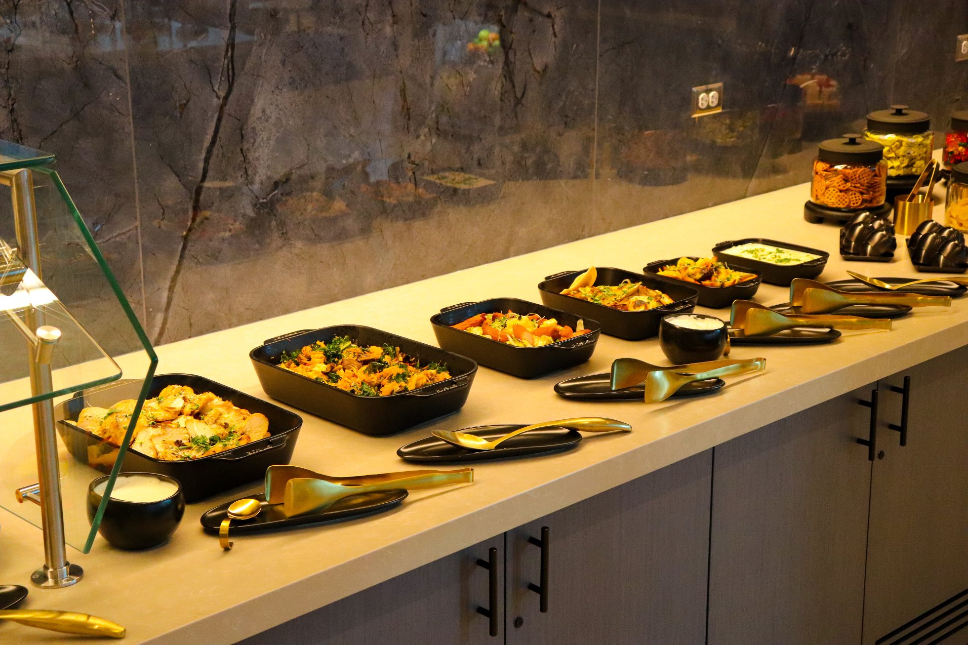 Swedish buffet with dishes served in black platters on white countertops - Business Lounge Chicago