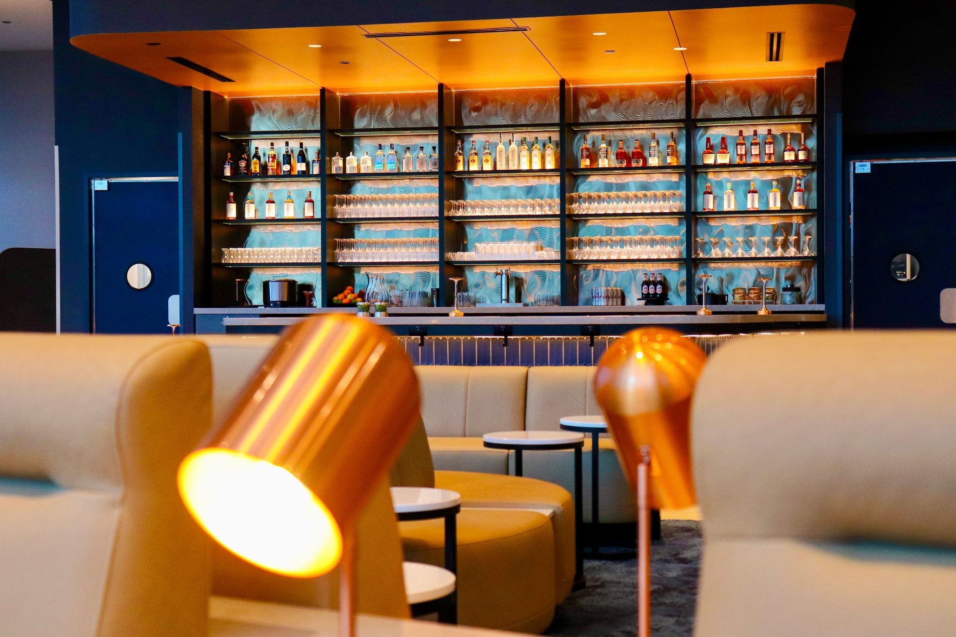 Close-up of armchairs and lighting between them, with a lit bar in the background of a business lounge in Chicago