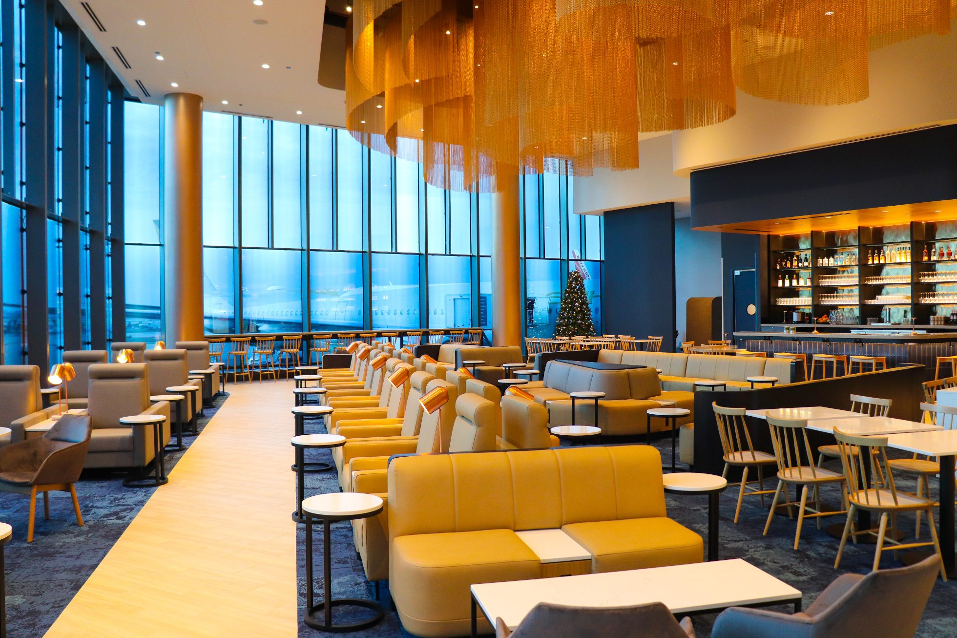 Spacious, elegant Chicago business lounge interior: beige sofas, stylish lighting, large panoramic window with airfield view.