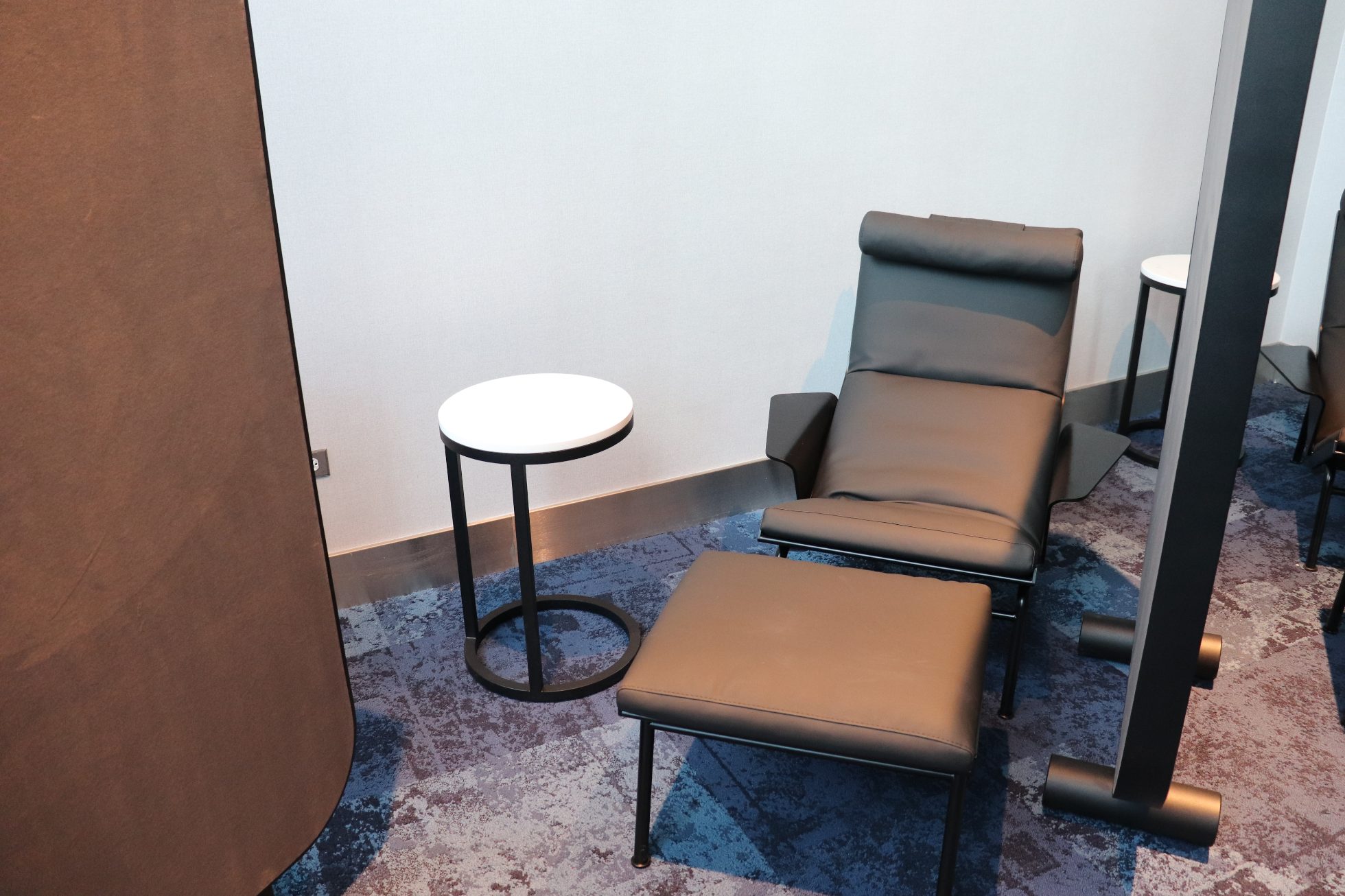 Individual space - black armchair with footrest and round table, warm lighting.