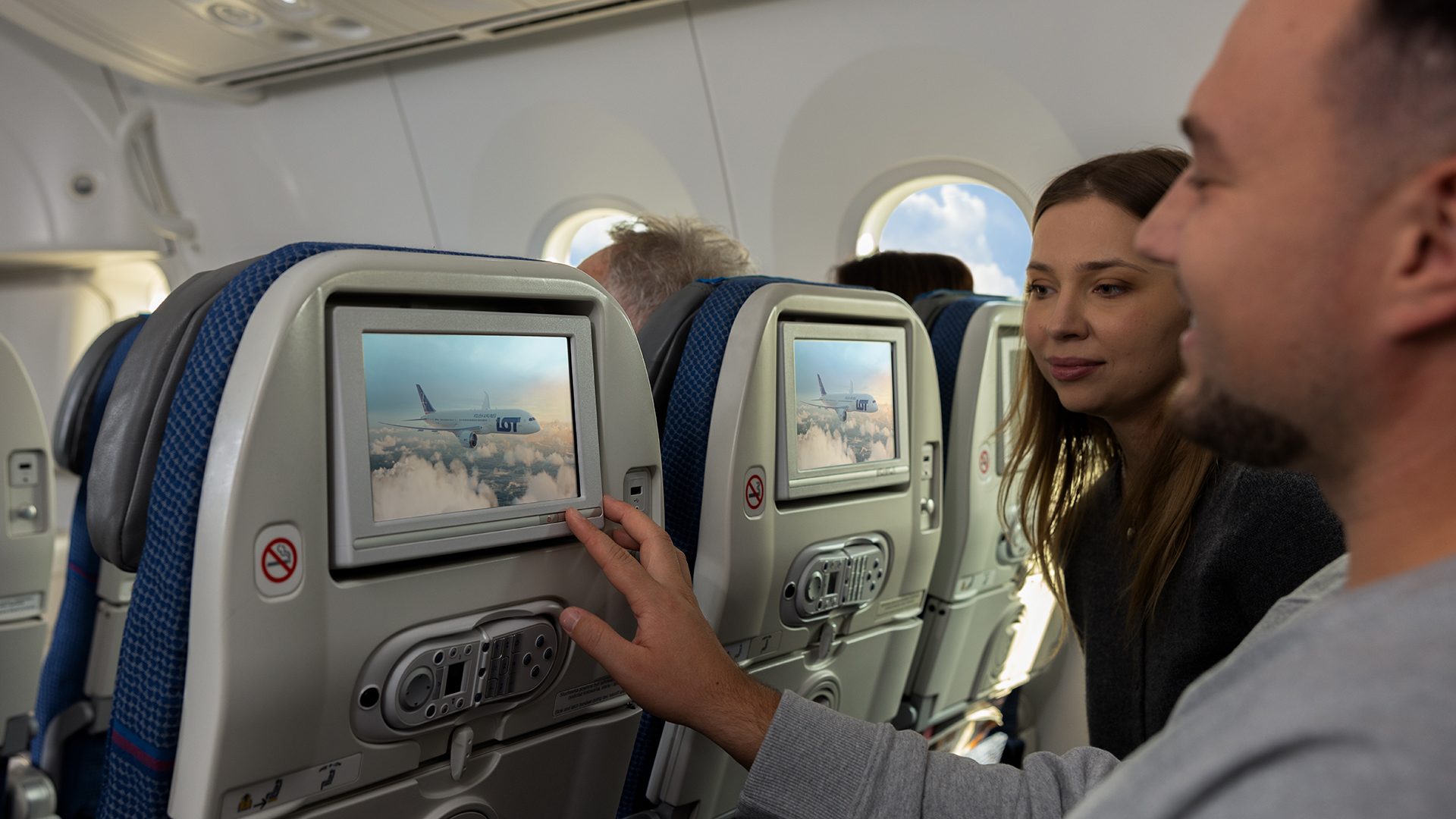Pasażerowie na pokładzie Dreamlinera w klasie ekonomicznej sprawdzają coś na ekranie zamontowanym w siedzeniu.