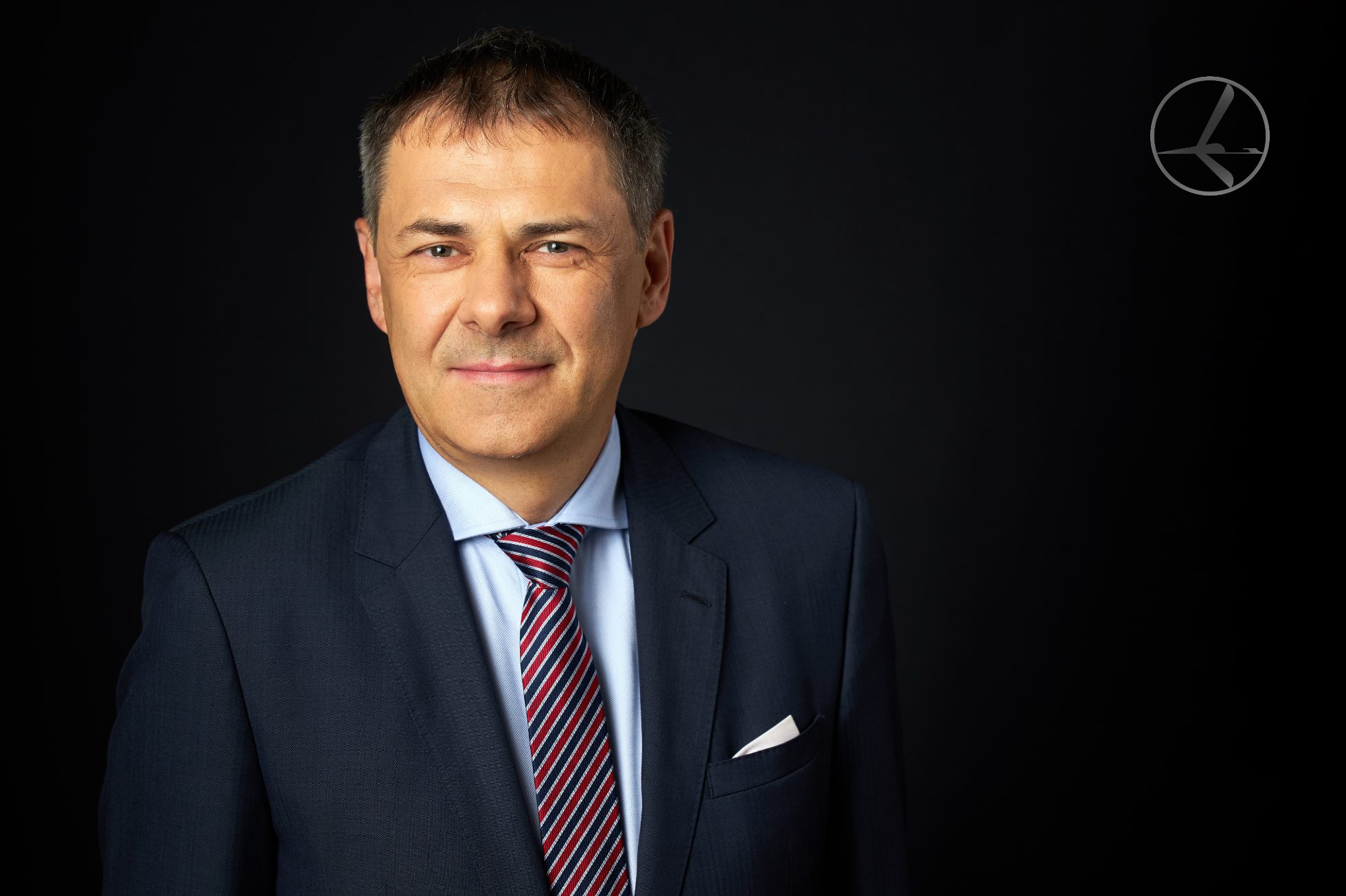 A man in a suit sits on a chair and looks at the camera.