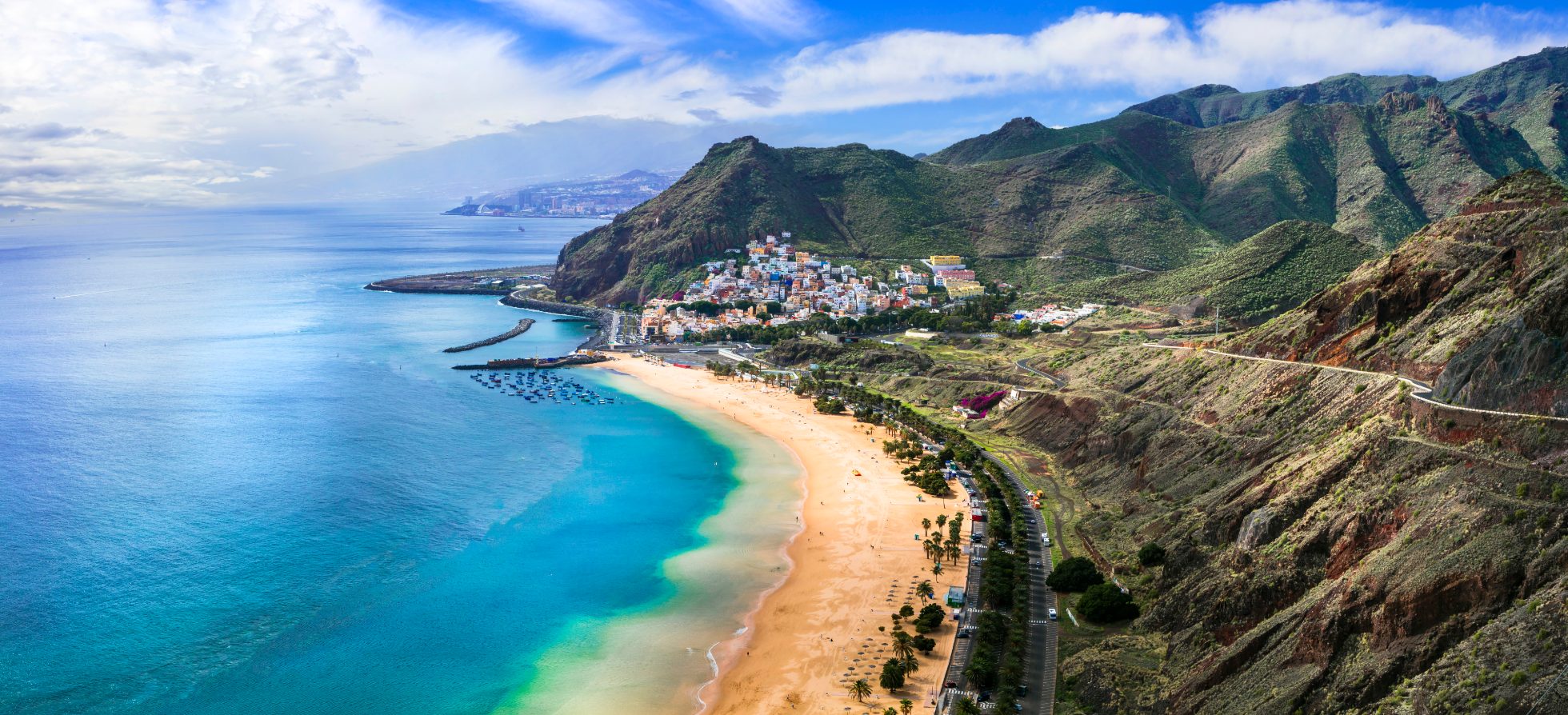 Beautiful beach with blue sea, golden sand, and palm trees. Mountains in the background, clear sky.