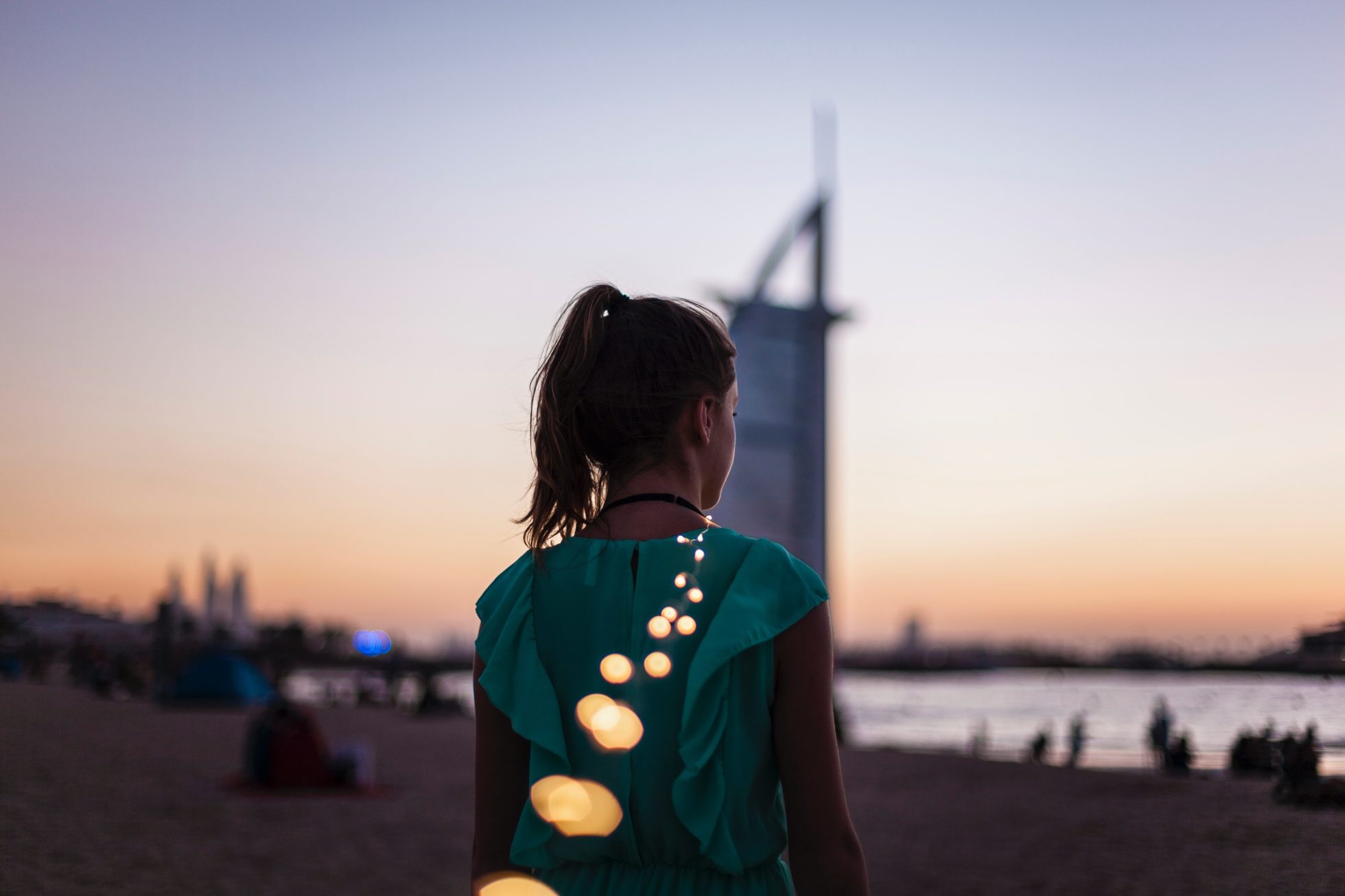 dziewczyna na plaży w Dubaju stojąca plecami do kamery o zachodzie słońca