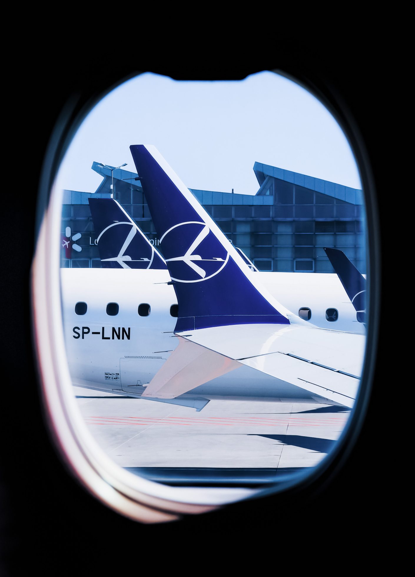 View through the window of the Boeing 737 MAX wing at Warsaw Chopin Airport and some other planes in the background