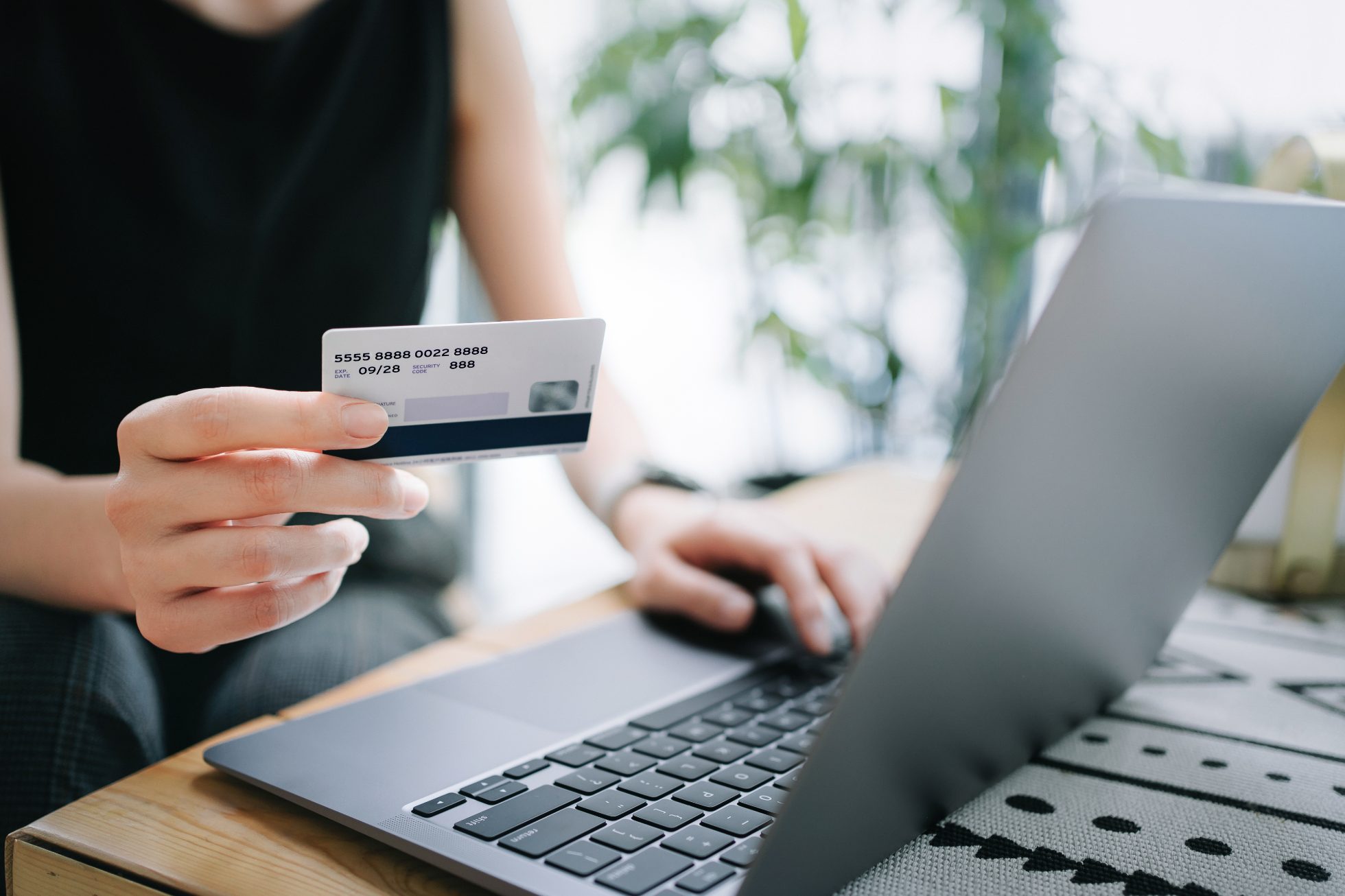 Zbliżenie na środkową część ciała młodej kobiety relaksującej się w kawiarni, robiącej zakupy online za pomocą laptopa i dokonującej płatności mobilnej kartą kredytową w ręku. 