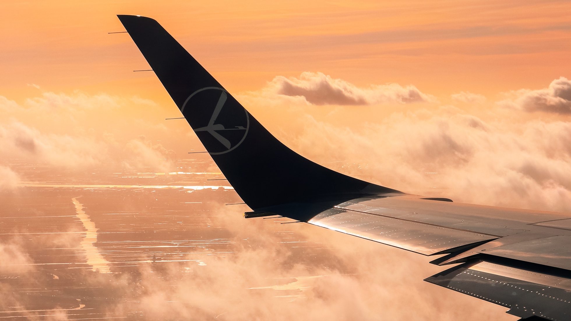 Airplane wing, clouds and orange sky during landing in Amsterdam