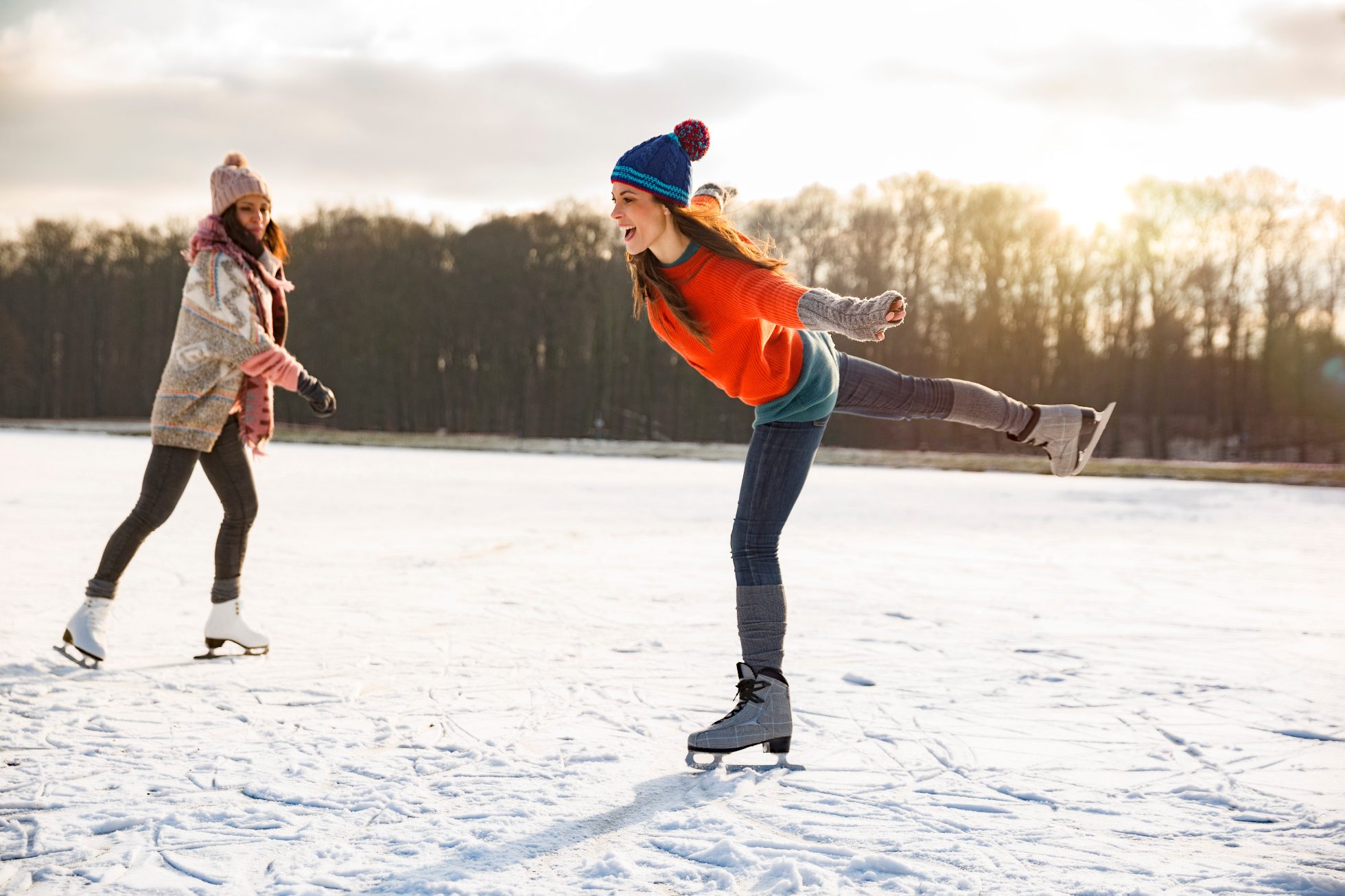 uśmiechnięte kobiety podczas jazdy na łyżwach na zamarźniętym jeziorze, sporty zimowe