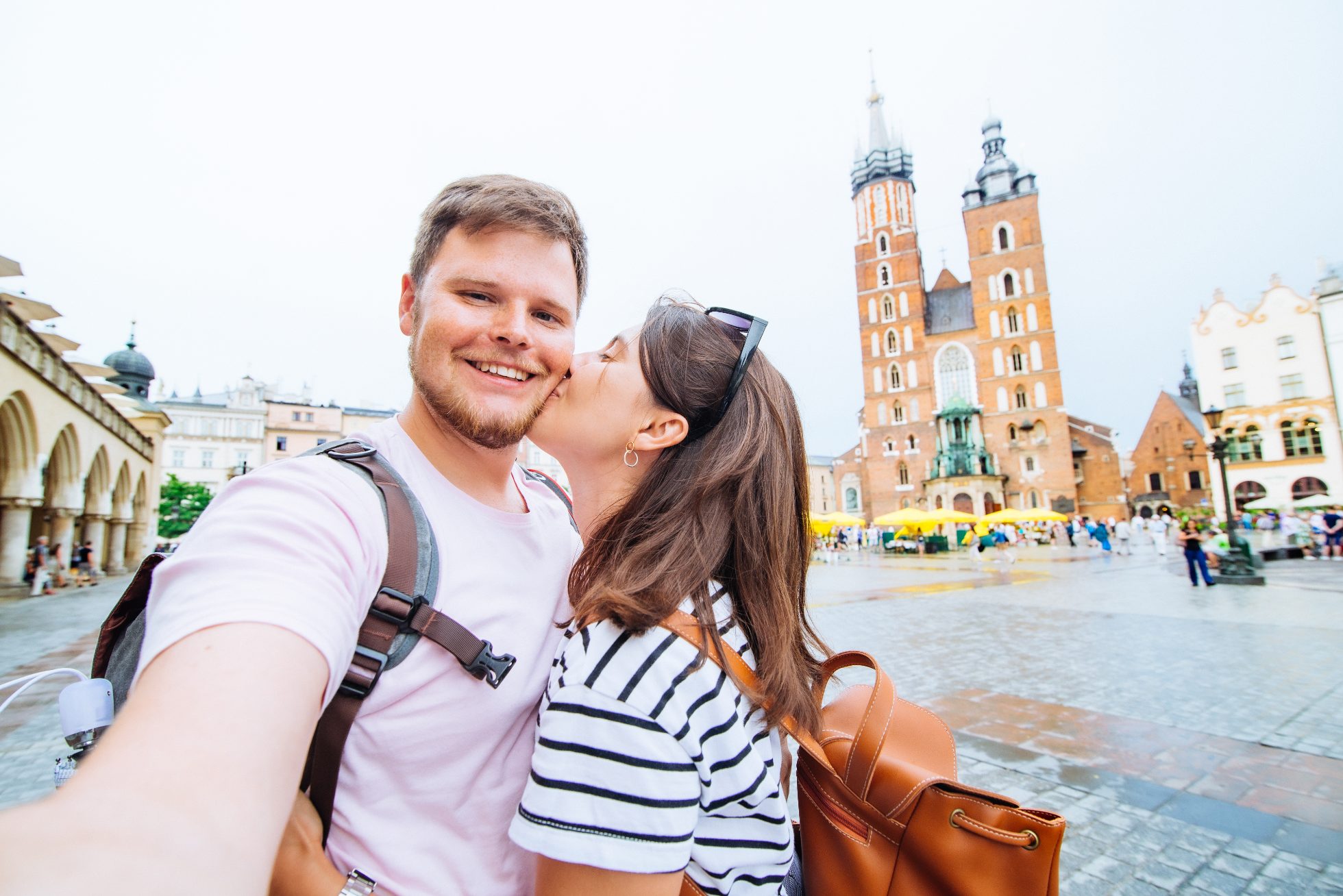 A happy couple. The woman gives the man a kiss on the cheek while he takes a selfie of them together.