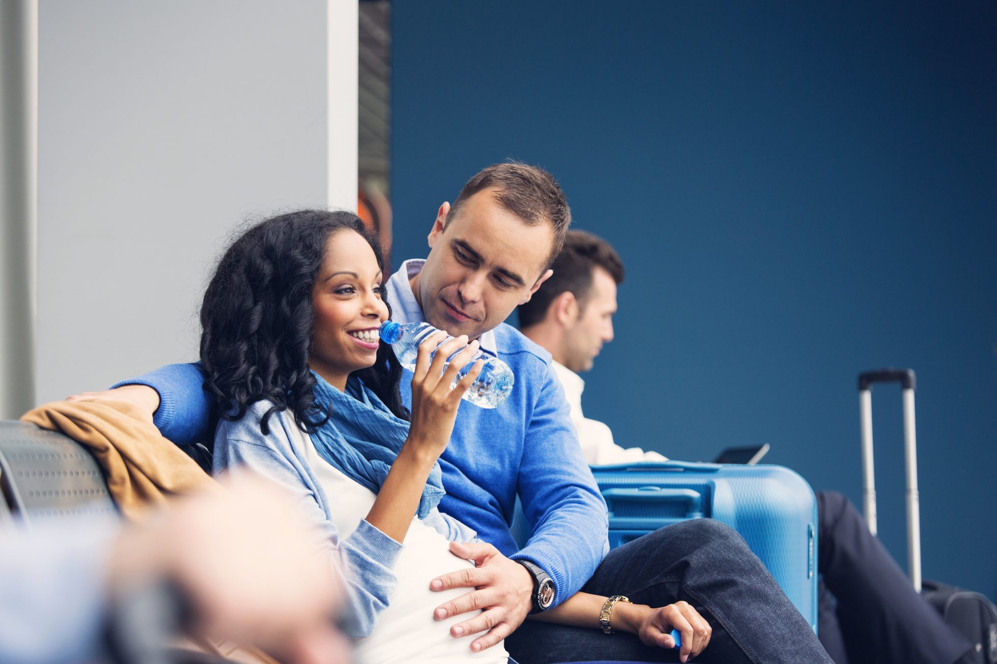 A happy pregnant woman waits with her partner for a flight in the airport lounge, drinking mineral water, flying on a plane while pregnant