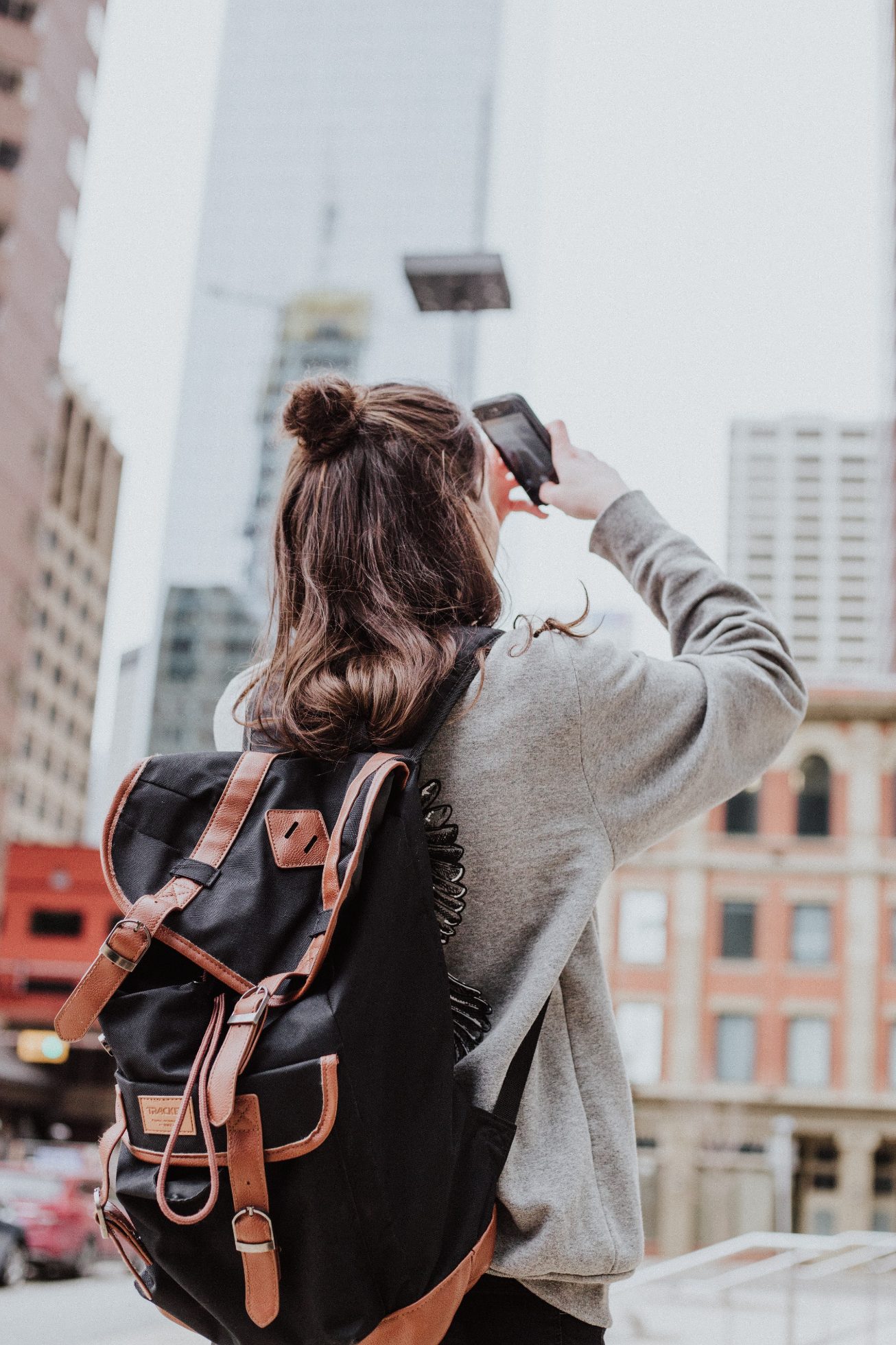 A woman with a backpack taking photos of the city skyline with her phone