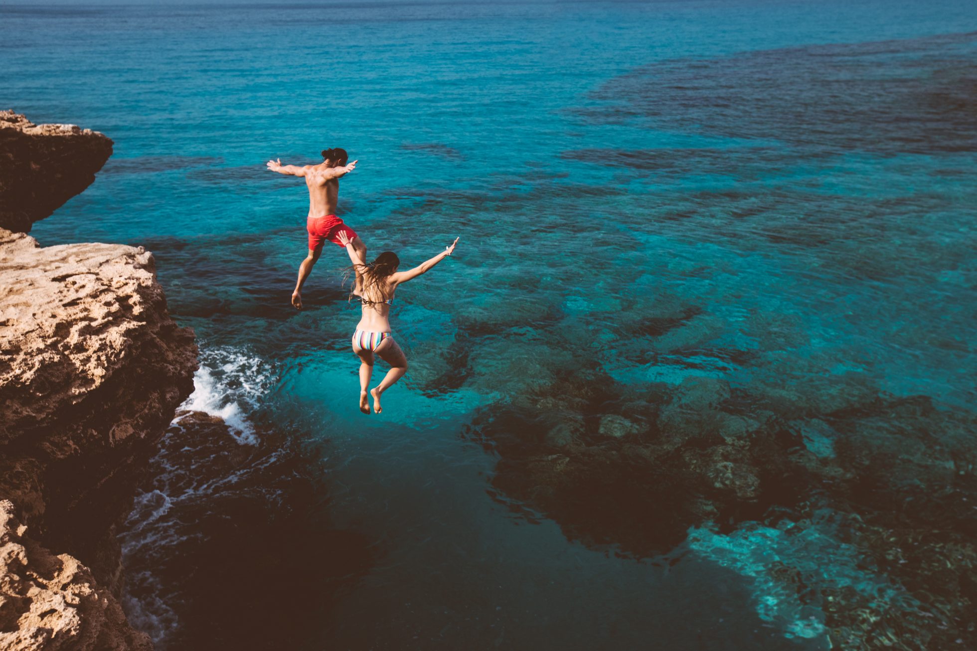 Two people jumping off a cliff into the sea