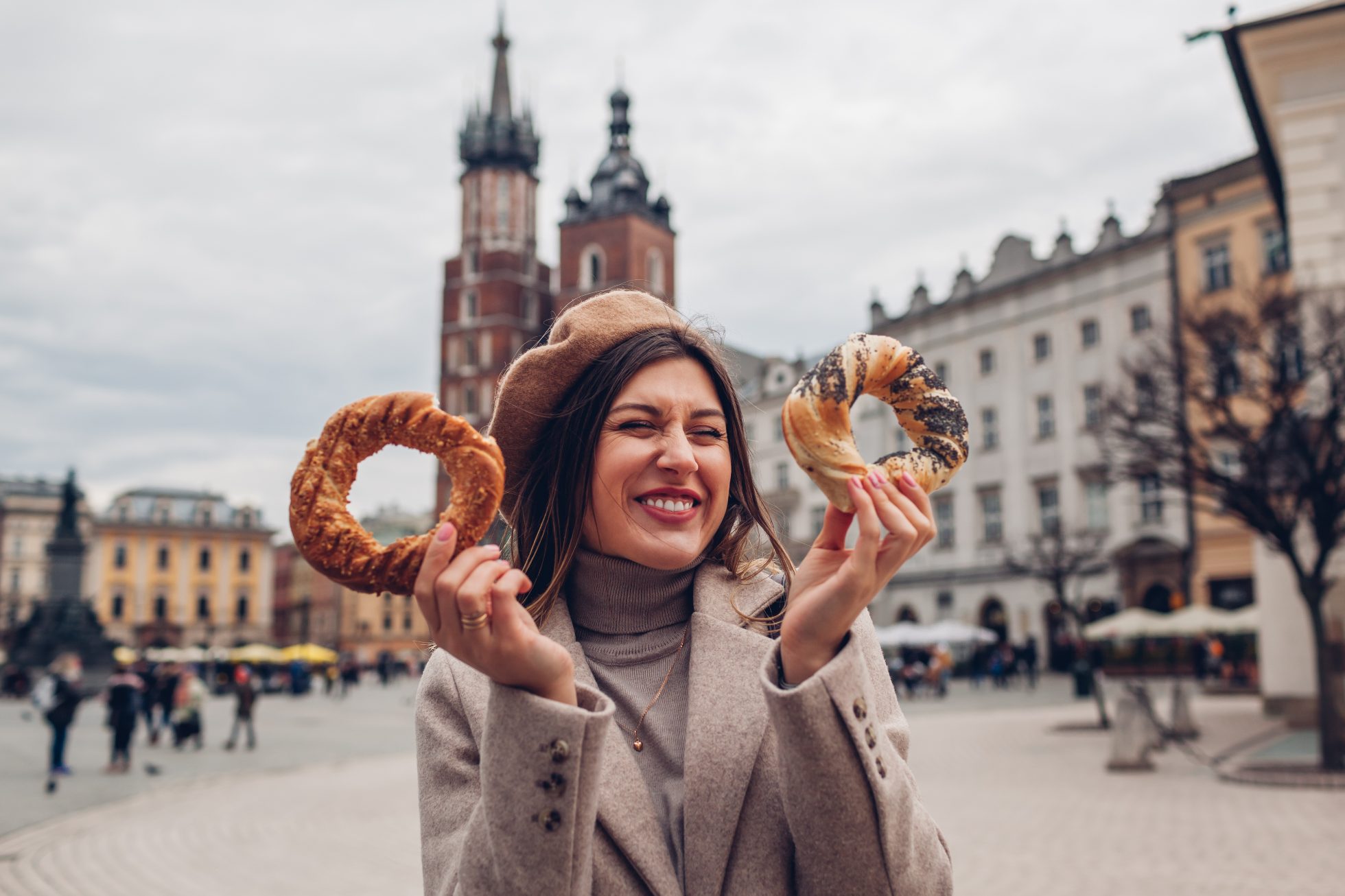 Tourist woman eating bagel obwarzanek traditional polish cuisine snack waling on Market square in Krakow.