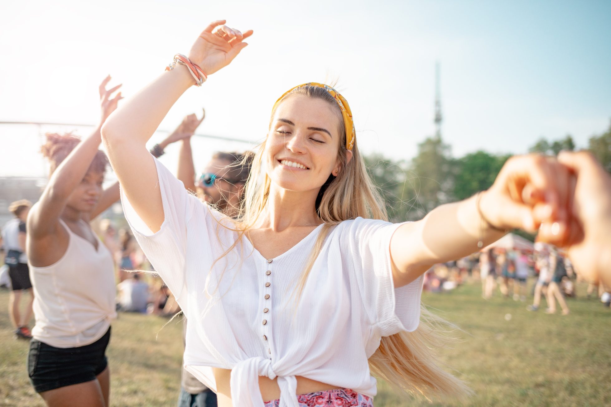 Piękna młoda długowłosa kobieta tańczy z przyjaciółmi na świeżym powietrzu na festiwalu muzycznym