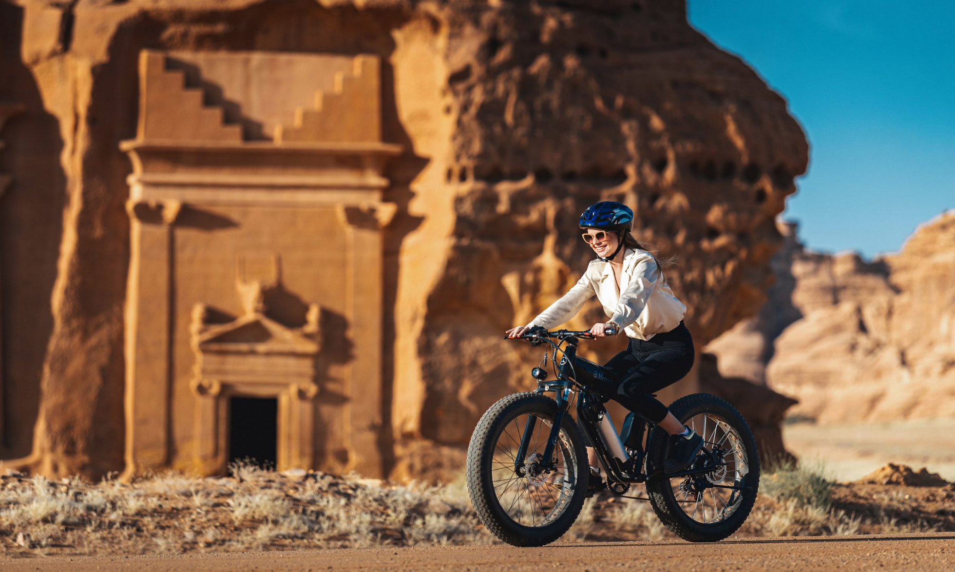 A woman on a bicycle riding past ancient tombs in AlUla