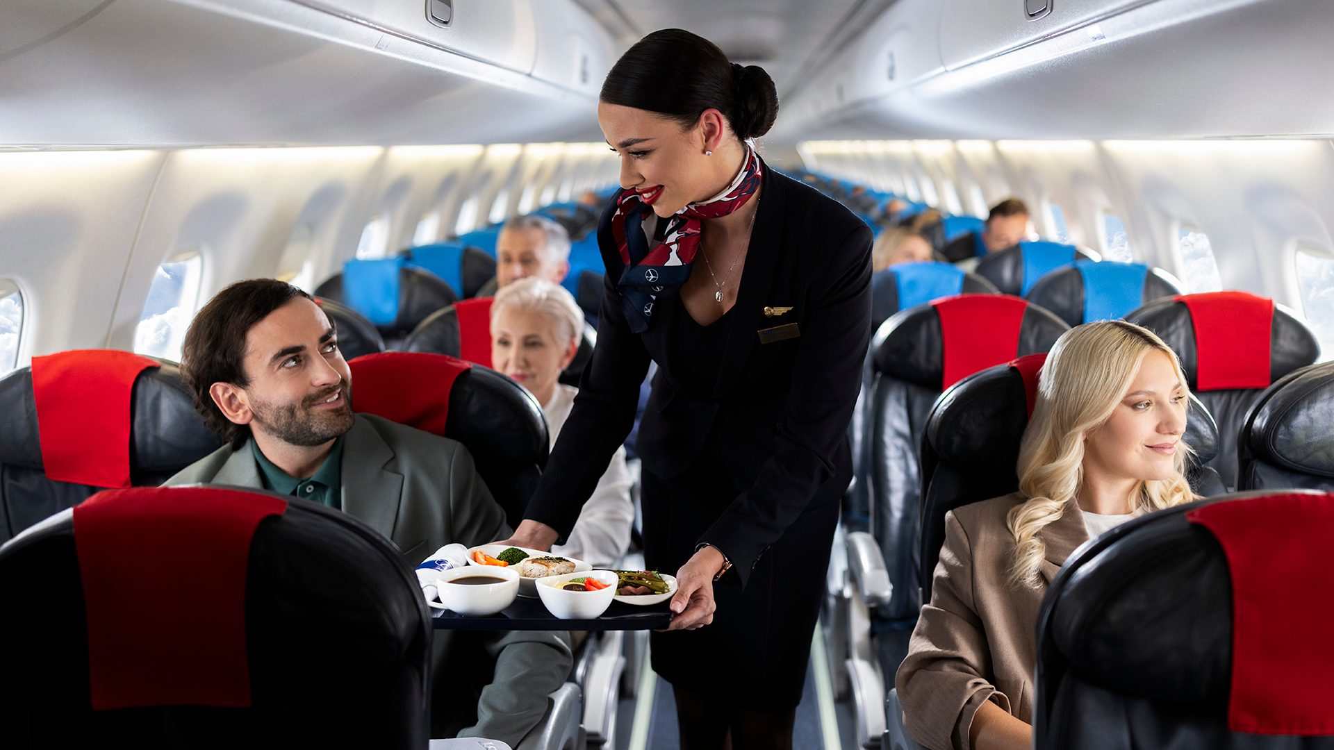 A stewardess serves food to a passenger aboard an Embraer