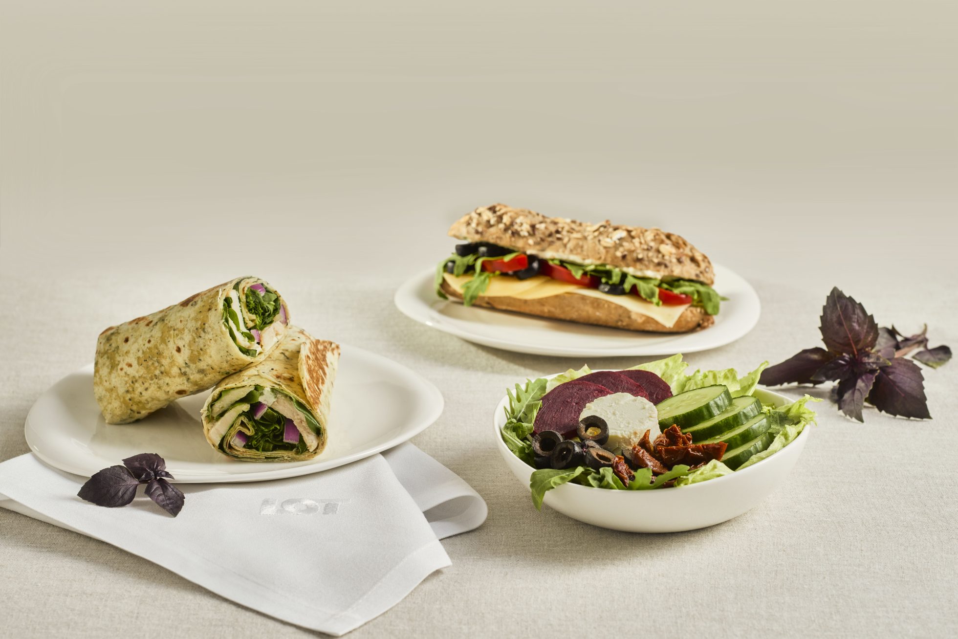 Salads, wraps, sandwiches on a wooden table.